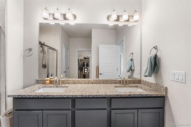 bathroom featuring double vanity, a shower stall, a spacious closet, and a sink