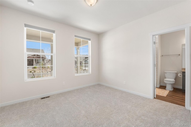 unfurnished bedroom with carpet, ensuite bath, visible vents, and baseboards
