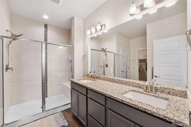 bathroom with a sink, double vanity, a shower stall, and wood finished floors