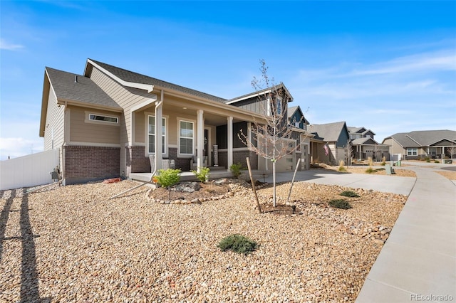 craftsman inspired home with driveway, brick siding, fence, a residential view, and a porch