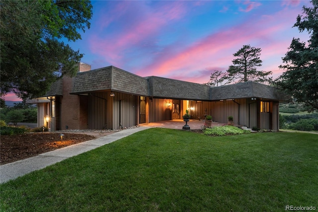 view of front facade with board and batten siding, a front lawn, roof with shingles, mansard roof, and a patio