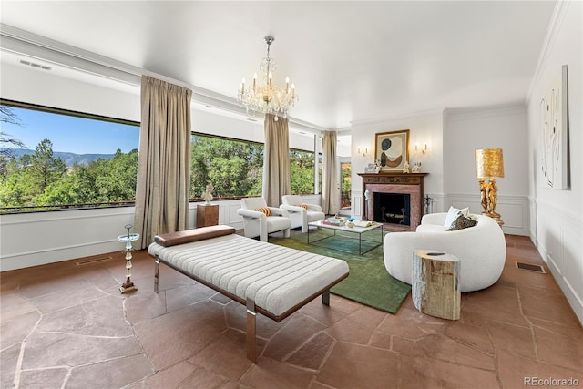 living room with stone tile floors, a wainscoted wall, an inviting chandelier, a fireplace, and crown molding