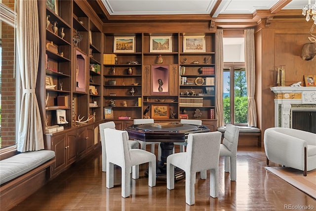 dining space featuring built in shelves, dark wood-style floors, a premium fireplace, ornamental molding, and wood walls