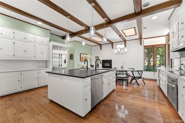 kitchen featuring light wood finished floors, a sink, beam ceiling, appliances with stainless steel finishes, and a kitchen island with sink