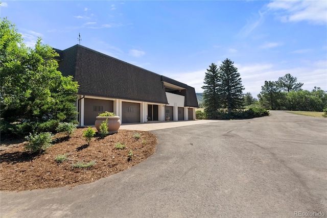 view of front of house featuring community garages, mansard roof, and a shingled roof