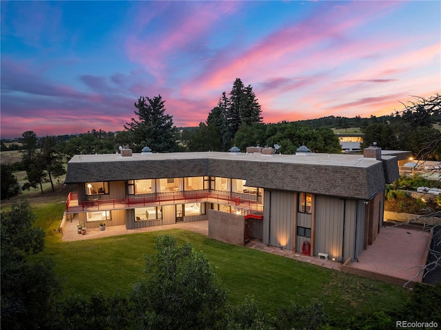 back of house at dusk with a patio, an outbuilding, a lawn, and a shingled roof