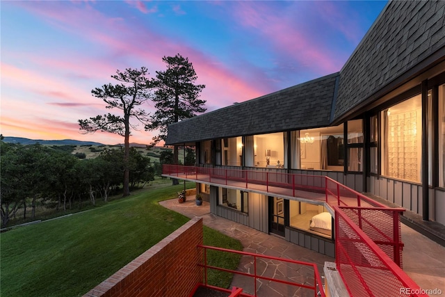 back of property at dusk featuring mansard roof, a lawn, a mountain view, and a shingled roof