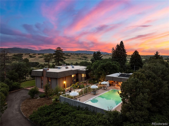 back of property at dusk featuring a patio, a fenced in pool, a mountain view, and stucco siding