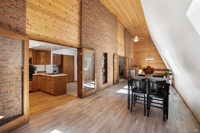 dining space with brick wall, a towering ceiling, wood walls, ceiling fan with notable chandelier, and light wood-type flooring