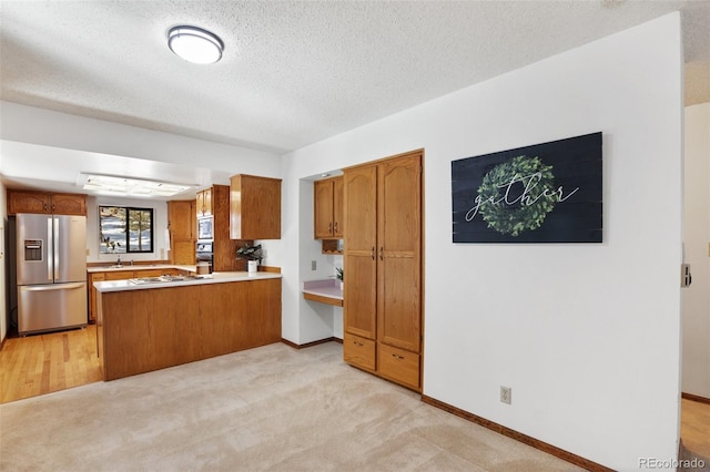 kitchen with brown cabinets, appliances with stainless steel finishes, a textured ceiling, and a peninsula