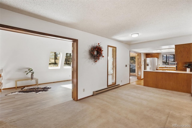 unfurnished living room featuring light colored carpet, a textured ceiling, a baseboard heating unit, and baseboards
