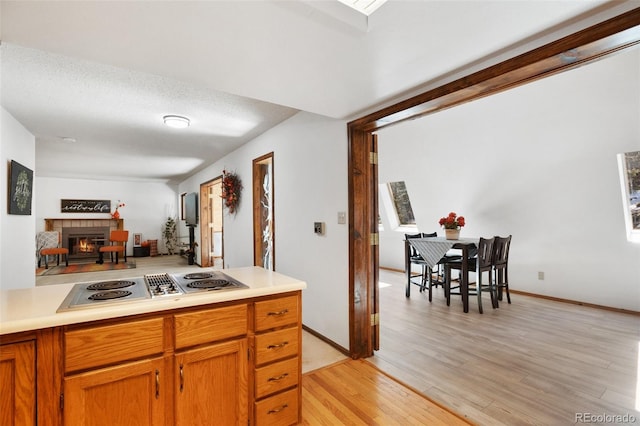 kitchen featuring light wood-style floors, stainless steel electric cooktop, a glass covered fireplace, and light countertops