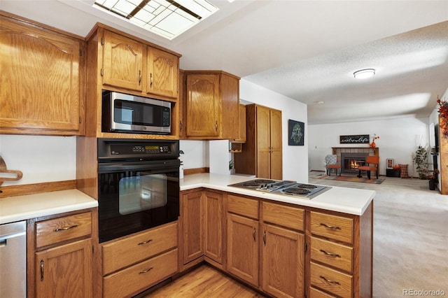 kitchen with brown cabinets, a glass covered fireplace, open floor plan, stainless steel appliances, and a peninsula