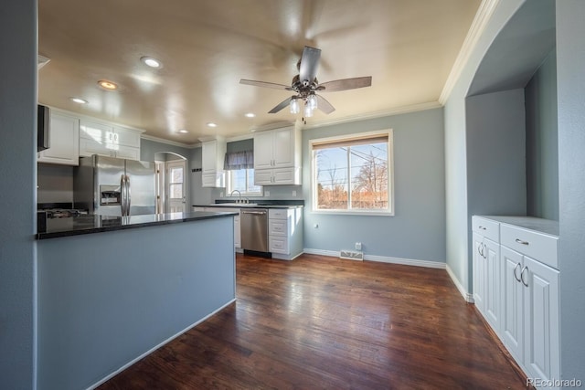 kitchen featuring dark countertops, appliances with stainless steel finishes, arched walkways, and crown molding