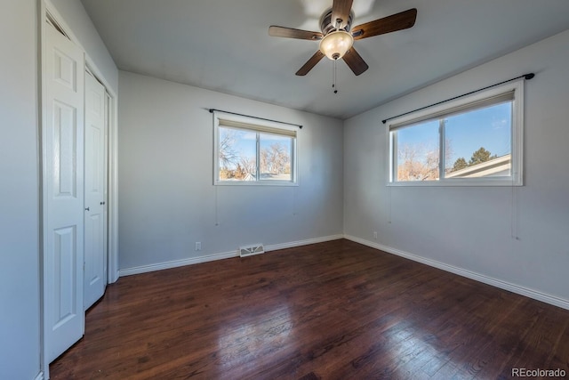 unfurnished bedroom with multiple windows, dark wood finished floors, and baseboards