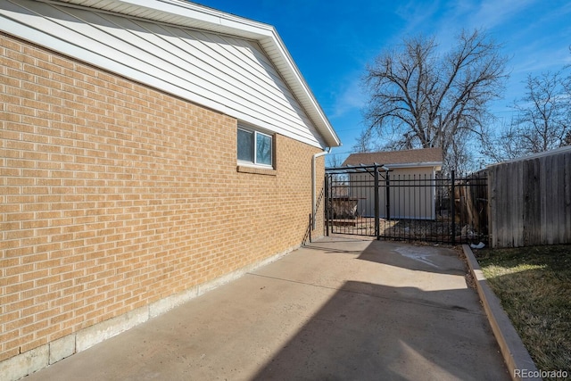 view of property exterior featuring brick siding, fence, and a gate