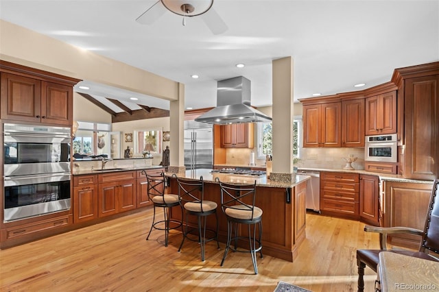 kitchen with sink, appliances with stainless steel finishes, a center island, light stone countertops, and island exhaust hood