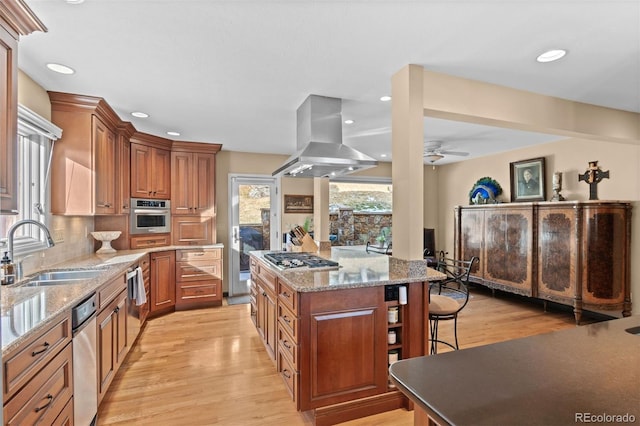 kitchen with sink, stainless steel appliances, a center island, island range hood, and light wood-type flooring