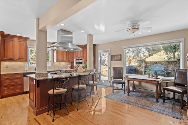 kitchen featuring island exhaust hood, a breakfast bar, light stone countertops, and light wood-type flooring