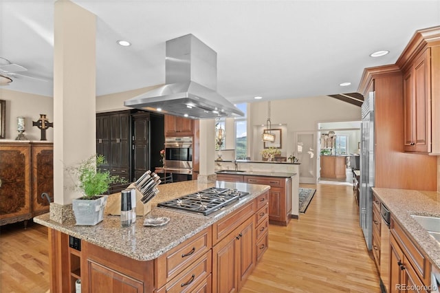 kitchen featuring light stone countertops, island exhaust hood, appliances with stainless steel finishes, and light hardwood / wood-style flooring