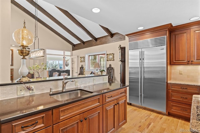 kitchen featuring stainless steel built in refrigerator, sink, dark stone countertops, and vaulted ceiling with beams