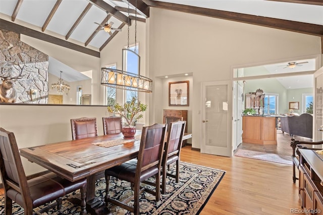dining space with vaulted ceiling with beams, ceiling fan with notable chandelier, and light wood-type flooring