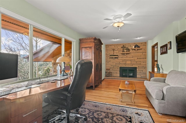 office with ceiling fan, a stone fireplace, and light wood-type flooring