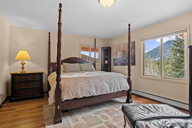 bedroom featuring baseboard heating, a mountain view, light hardwood / wood-style floors, and multiple windows