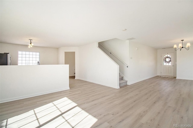 unfurnished living room featuring light hardwood / wood-style flooring, a notable chandelier, and plenty of natural light