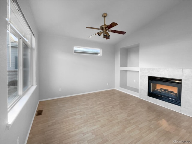 unfurnished living room featuring light hardwood / wood-style floors, built in features, a tile fireplace, and vaulted ceiling