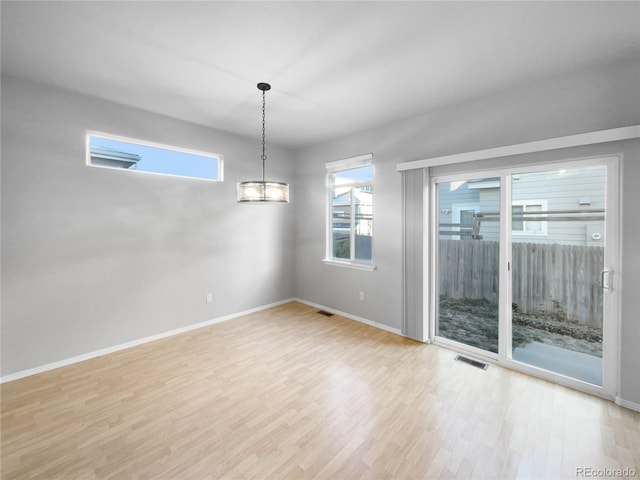 empty room featuring a chandelier, light hardwood / wood-style flooring, and a healthy amount of sunlight