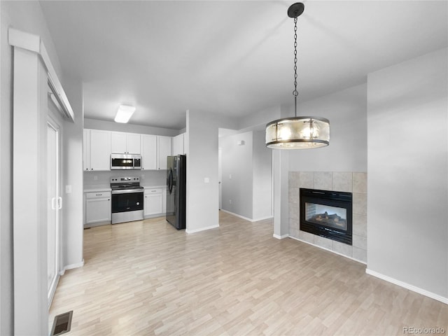 kitchen featuring a tile fireplace, hanging light fixtures, stainless steel appliances, white cabinets, and light wood-type flooring