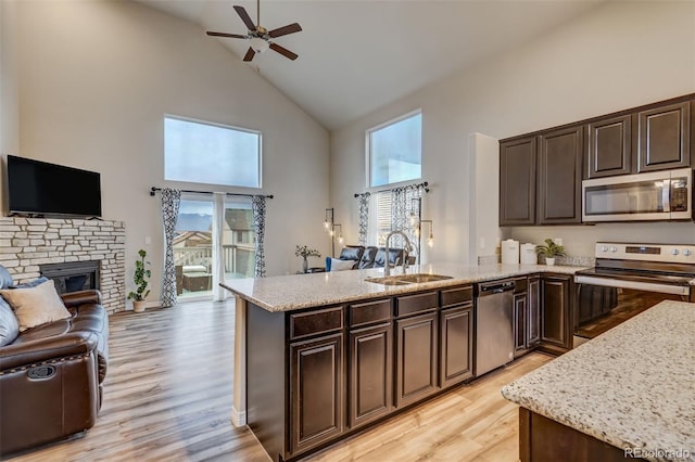 kitchen with stainless steel appliances, sink, high vaulted ceiling, a fireplace, and light hardwood / wood-style floors