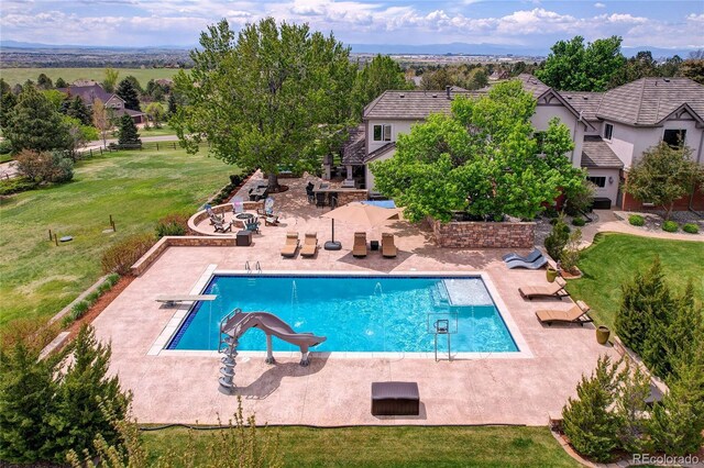 outdoor pool featuring a water slide, a patio area, a yard, and a diving board
