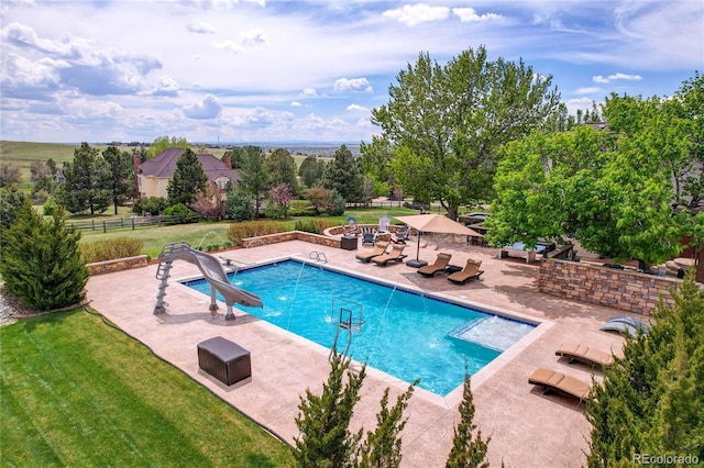 outdoor pool featuring a patio, a water slide, and view of wooded area