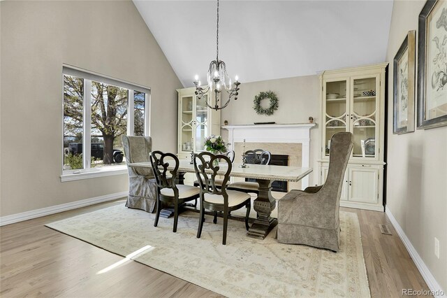 dining area featuring wood finished floors, a chandelier, baseboards, high vaulted ceiling, and a high end fireplace