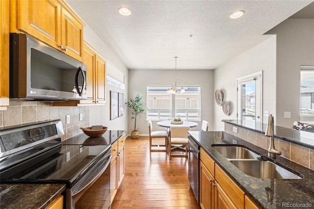 kitchen featuring light wood finished floors, a sink, dark stone counters, decorative backsplash, and appliances with stainless steel finishes