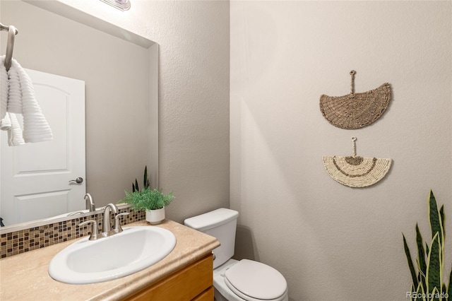 half bathroom with toilet, vanity, and tasteful backsplash