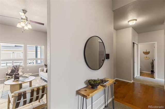 hallway featuring baseboards, wood finished floors, and a textured ceiling