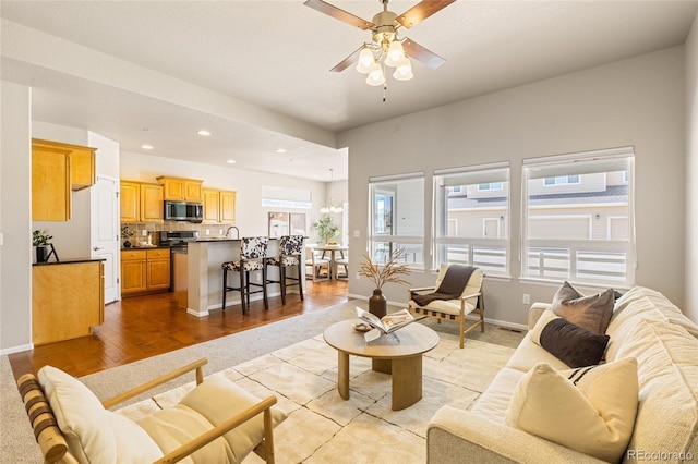 living room with baseboards, recessed lighting, light wood-style flooring, and ceiling fan with notable chandelier