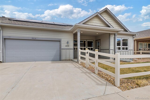 single story home featuring roof mounted solar panels, an attached garage, driveway, and fence