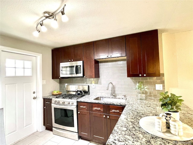 kitchen featuring appliances with stainless steel finishes, a sink, decorative backsplash, and light stone countertops