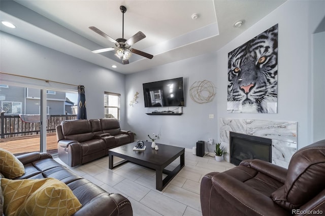 living room with ceiling fan, a high end fireplace, and a tray ceiling