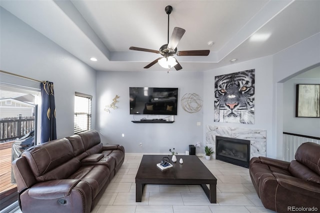 living room with a raised ceiling, ceiling fan, and a fireplace