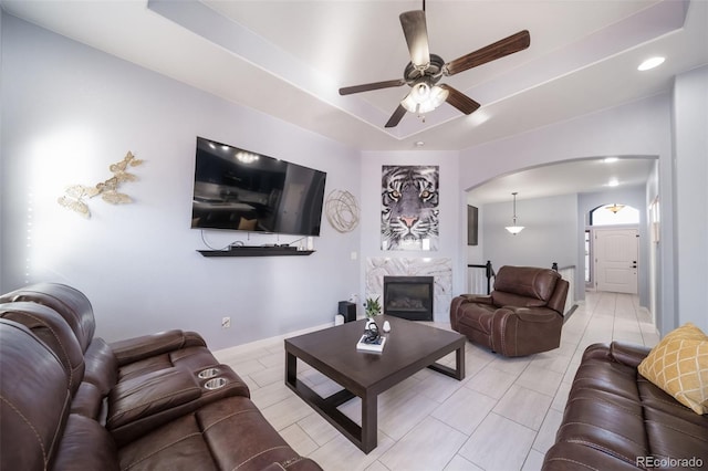 living room with a fireplace, a raised ceiling, ceiling fan, and light tile patterned flooring