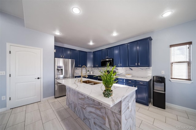 kitchen featuring blue cabinets, sink, a center island with sink, appliances with stainless steel finishes, and light stone countertops