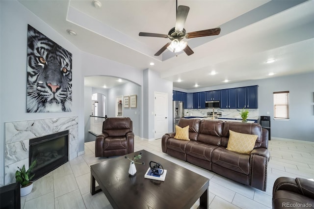 tiled living room featuring a tray ceiling, a high end fireplace, and ceiling fan