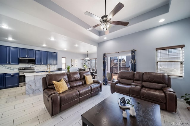 living room featuring ceiling fan, a raised ceiling, and sink