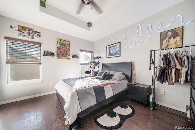 bedroom featuring multiple windows, dark hardwood / wood-style floors, ceiling fan, and a tray ceiling