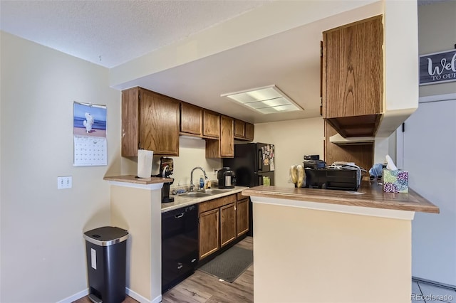 kitchen featuring black appliances, a sink, a textured ceiling, a peninsula, and light wood finished floors